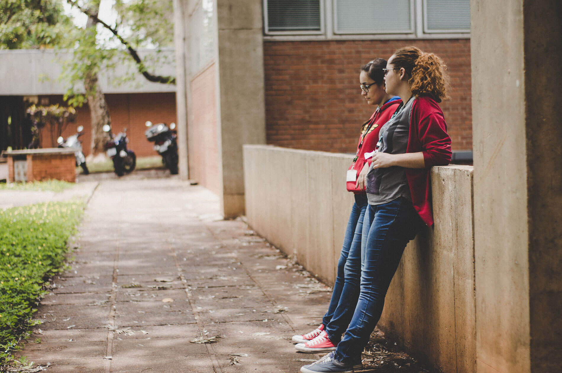 Two people leaning against a wall outdoors, engaged in conversation.